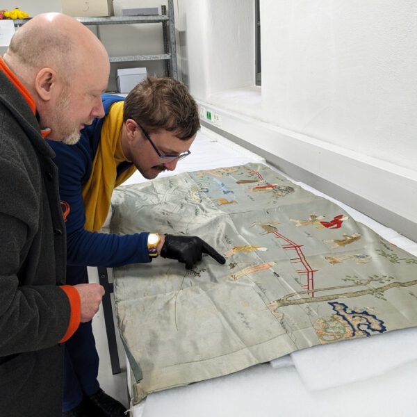Walter Bruno Brix und Constantijn Johannes Leliveld begutachten einen chinesischen Behang mit dem Motiv „Hundert spielende Knaben“. (© Museen Schloss Aschach, Foto: Josefine Glöckner)